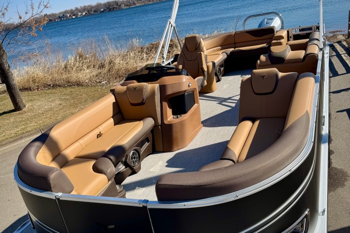 Tan and brown pontoon boat parked near a lake with clear blue sky.