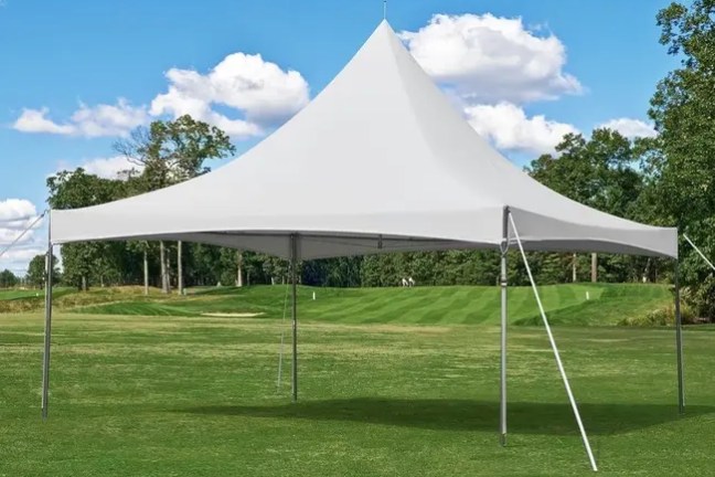 White tent on a grassy field with trees and blue sky in the background.